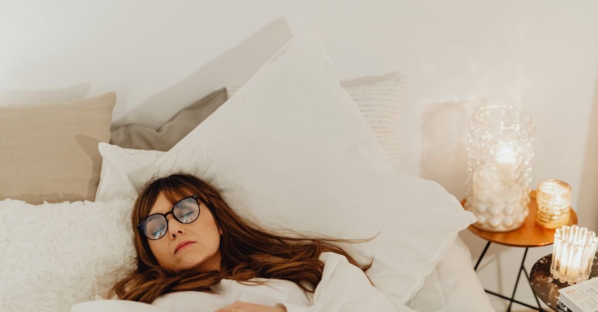 A woman peacefully resting in bed with dim lighting and soft white bedding.