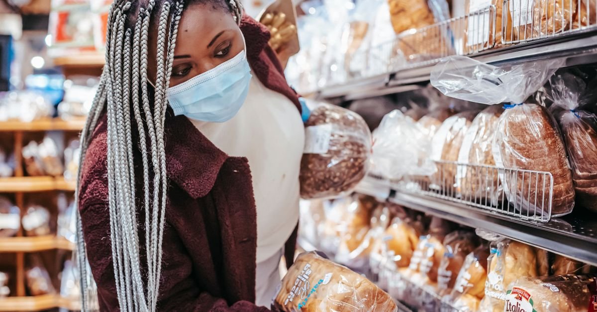 African American female customer in protective mask and gloves selecting bread in supermarket during coronavirus pandemic