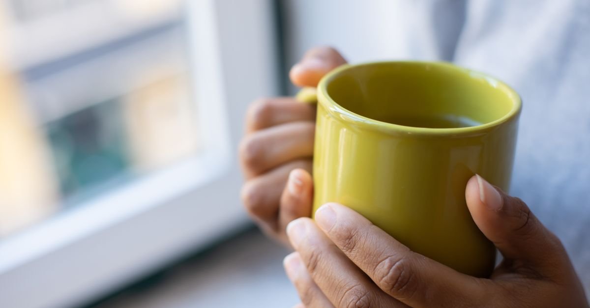 Close-up of hands holding a yellow mug near a window, creating a warm and cozy vibe.