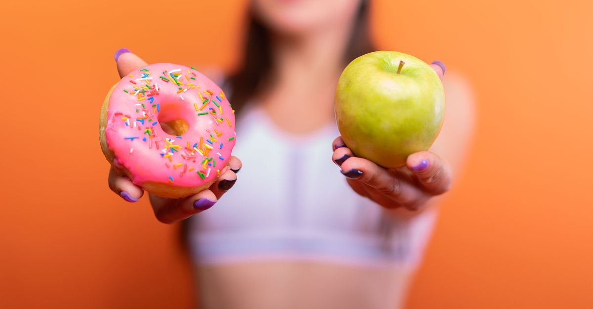 A woman holds a green apple and a pink donut with sprinkles against an orange background, emphasizing choice.