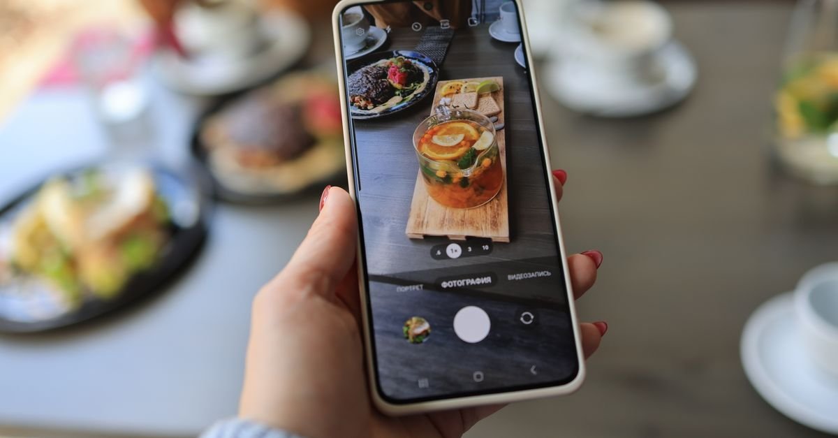 Close-up of hand holding smartphone photographing delicious meal on table.