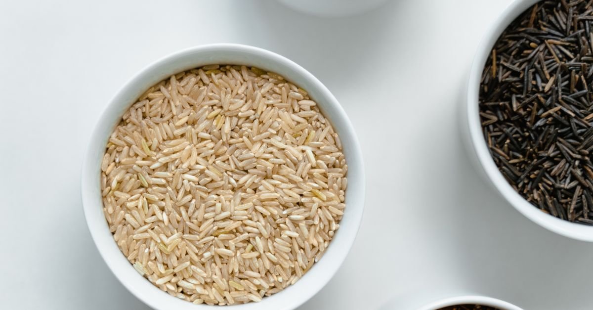 A variety of rice and grains displayed in white ceramic bowls on a clean white surface.