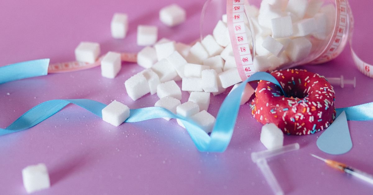 Creative representation of sugar consumption using cubes, donut, ribbon, and syringe.