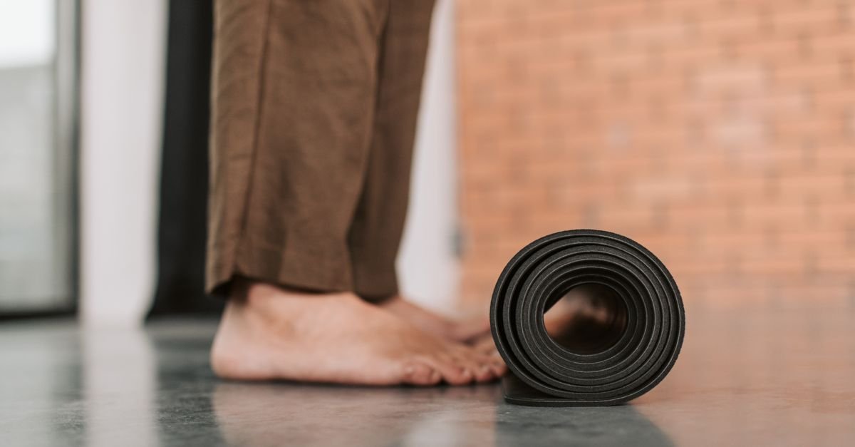 A person standing barefoot by a rolled yoga mat indoors, ready for exercise.