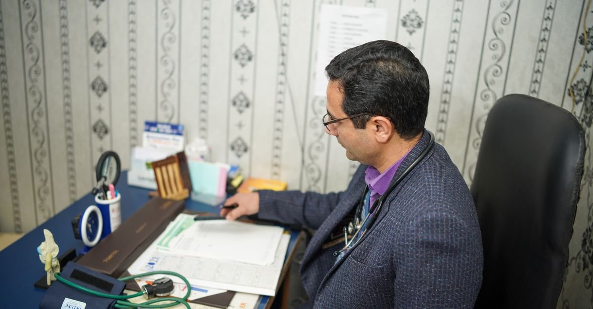 Doctor reviewing medical documents at desk in clinic office.