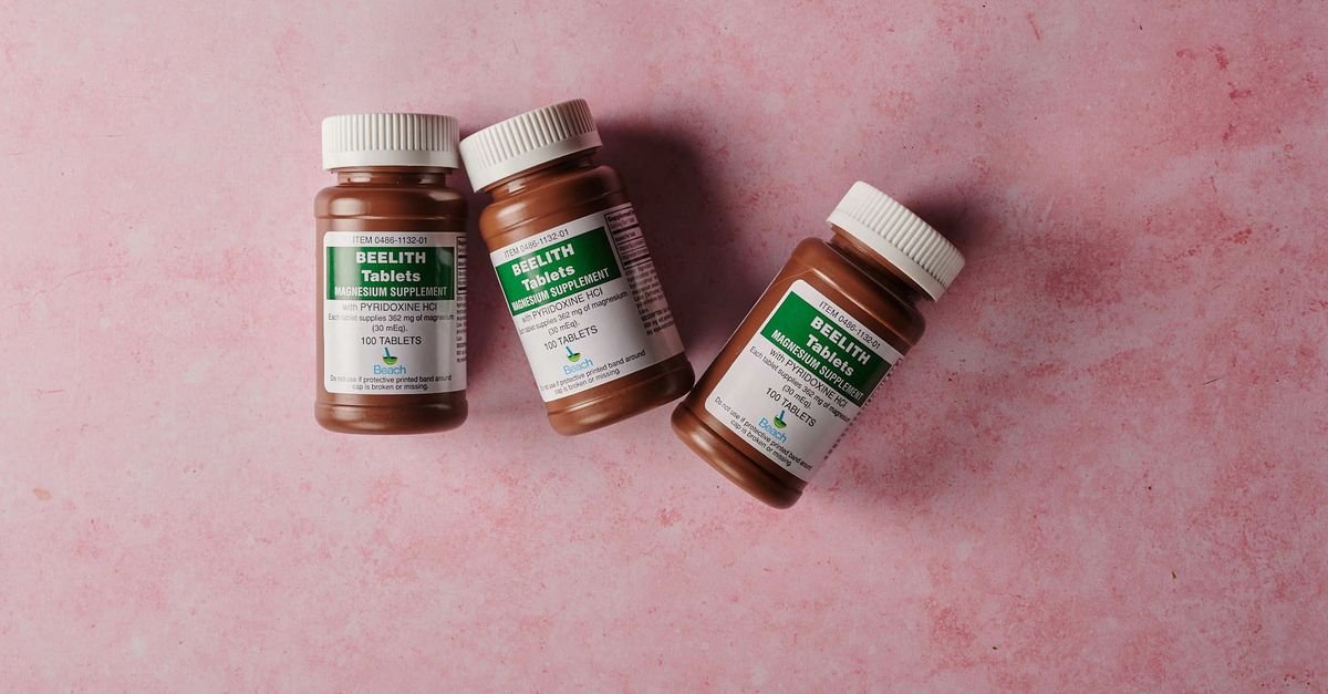 Three brown bottles of magnesium tablets on a soft pink background, ideal for health-themed content.