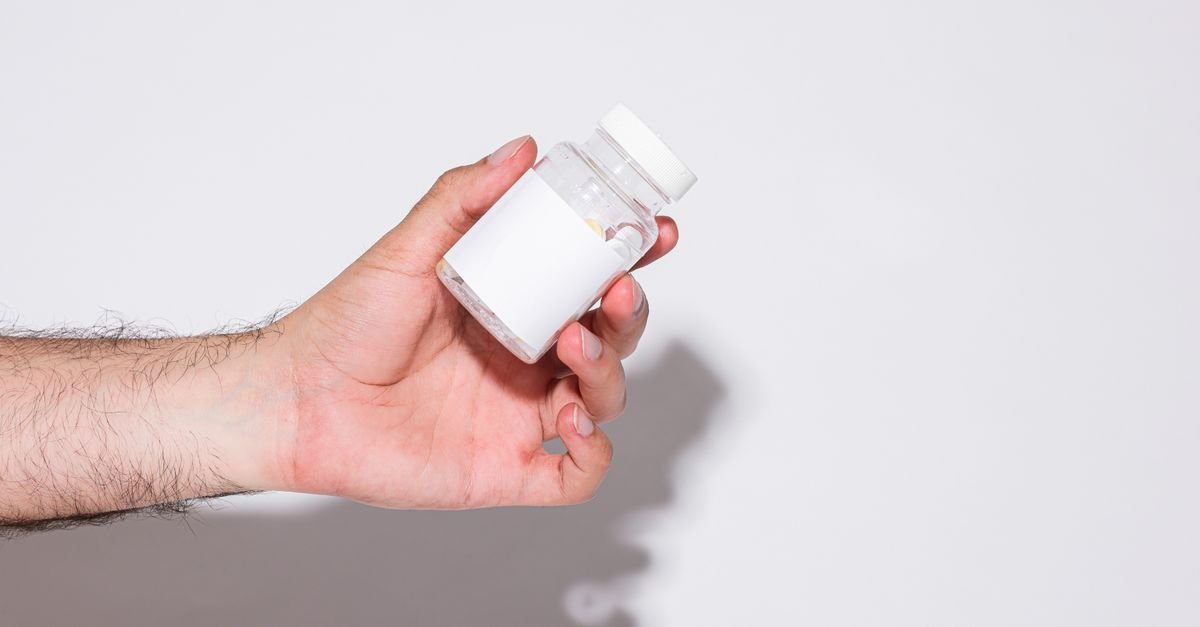 Close-up of a hand holding a small transparent plastic bottle against a bright white background.